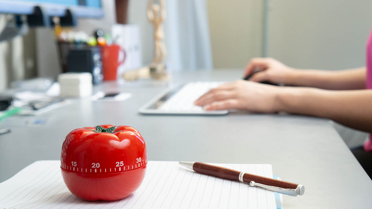 Person at computer with pomodoro timer on desk next to pen